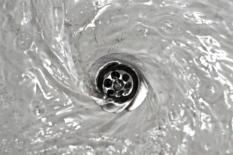 Water swirling down a metal sink drain, creating a visible vortex pattern, thanks to effective drain cleaning.