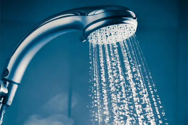 Close-up of water cascading from a showerhead against a blue background, showcasing the seamless flow that comes with expert tankless water heater repair.