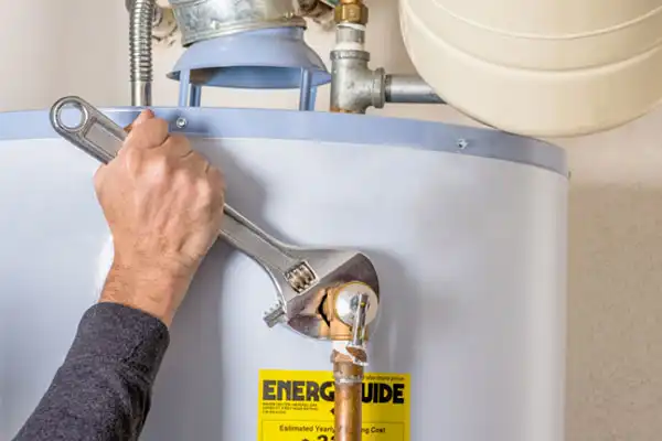 The person expertly uses a wrench to adjust the fittings on a water heater with an EnerGuide label, showcasing their skill in water heater repair.