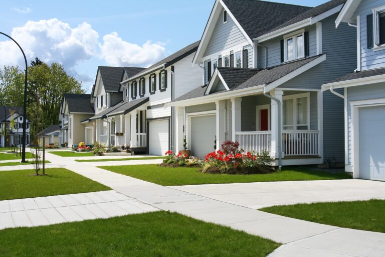 A row of modern suburban homes with neat lawns, driveways, and front porches lined along a street under a partly cloudy sky, while a downspout clearing service ensures everything stays pristine.